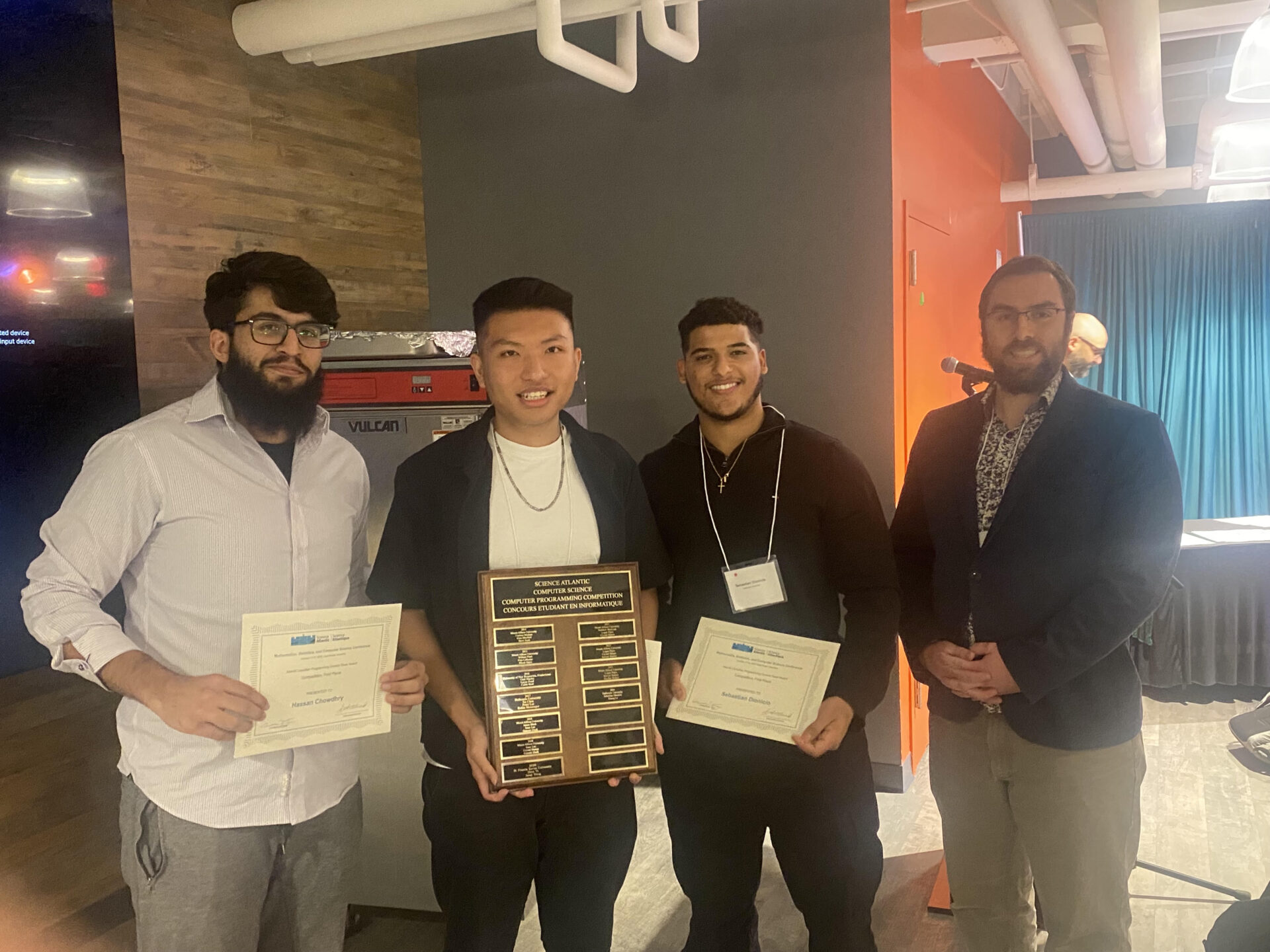 Four people standing smiling for a picture with certificates and a plaque for first place at the 2026 Science Atlantic Programming Competition